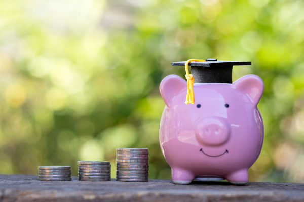 Photo of 3 stacks of coins sitting next to a piggy bank with a graduation cap on