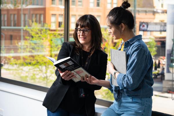 Two women leaning on a window reading a book 