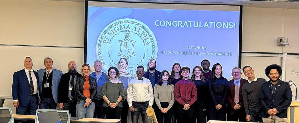 Photo of group of inductees into political science honor society.  Professors and students standing in a row in front of Pi Sigma Alpha logo.