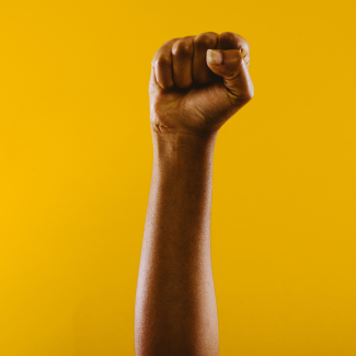 A protest fist raised to the sky with yellow background 