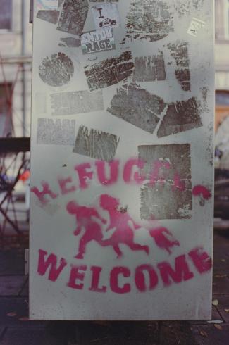 "Refugees Welcome" graffitied in pink spray paint on a cement wall