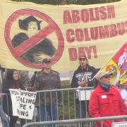 Protestors stand with signs reading Abolish Columbus Day