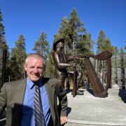 Jim Walsh smiling in front of memorial statue of a miner kneeling in front of a Celtic harp