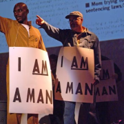 Two man wearning protest signs reading "I am a Man" and pointing off stage