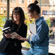 Two women leaning on a window reading a book 