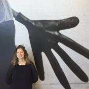 Tania Islas Weinstein in front of an artpiece displaying a large hand in black and white.
