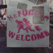 "Refugees Welcome" graffitied in pink spray paint on a cement wall