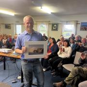 Jim Walsh holding art and smiling in front of dozens of clapping audience members