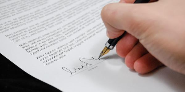 image of hand signing a piece of paper