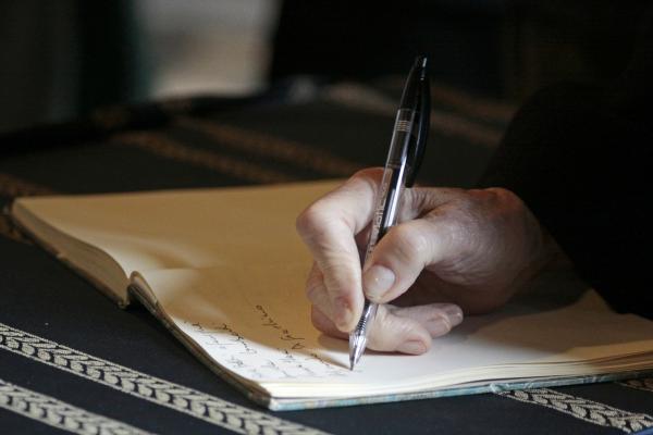 Image of a hand holding a pen and writing in a notebook