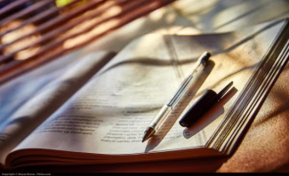 An open book with a pen and pen cap resting on the page and shadows on top